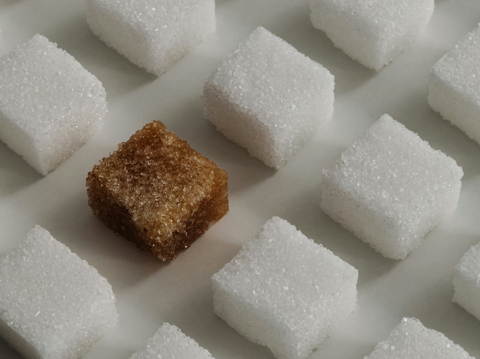 Weiße Zuckerwürfel im Raster mit einem braunen Rohrzuckerwürfel – Symbolbild für Blutzucker, Zuckerkonsum und Stoffwechsel