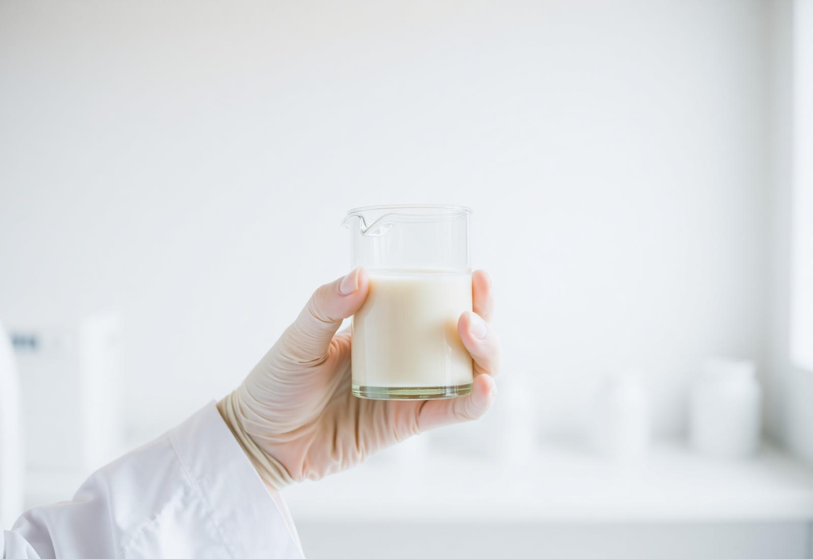 Laborhand hält ein Becherglas mit Milchprobe